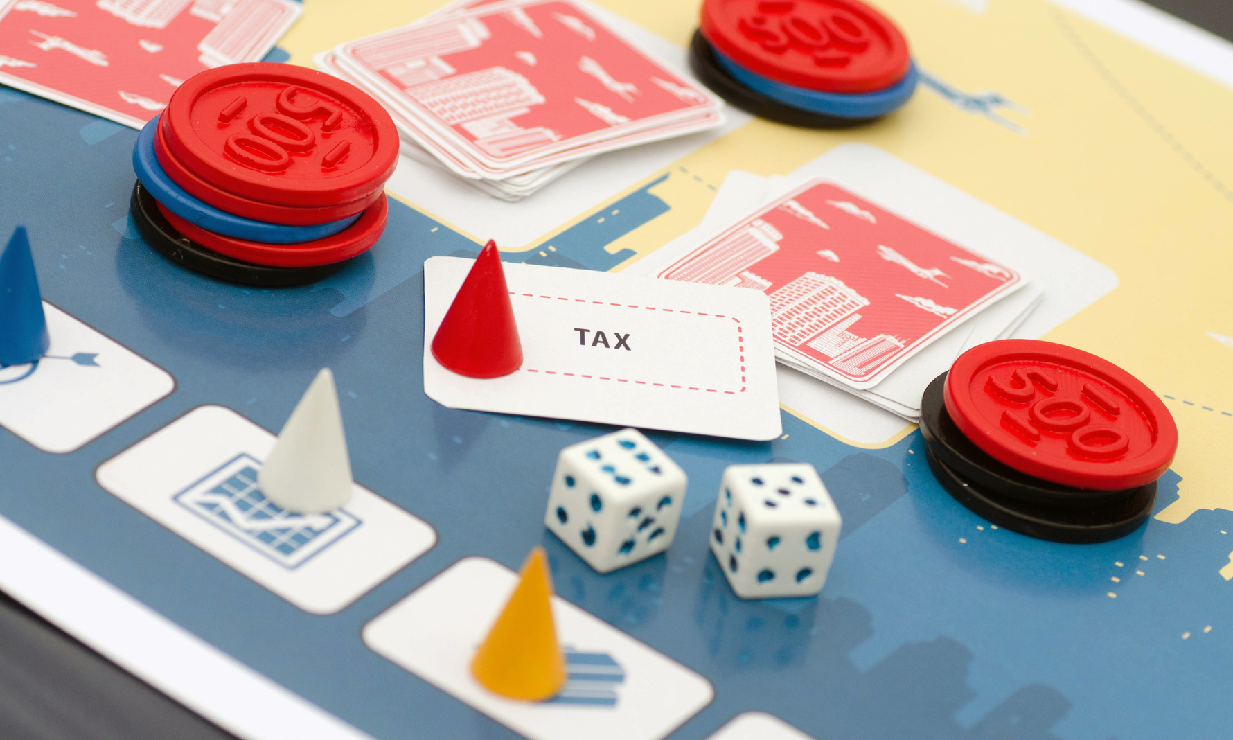 Board game prototype with cones, chips, dice, and card that says tax