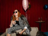 Chic redhead in sunglasses smoking a cigarette in a club alone with whiskey and balloons