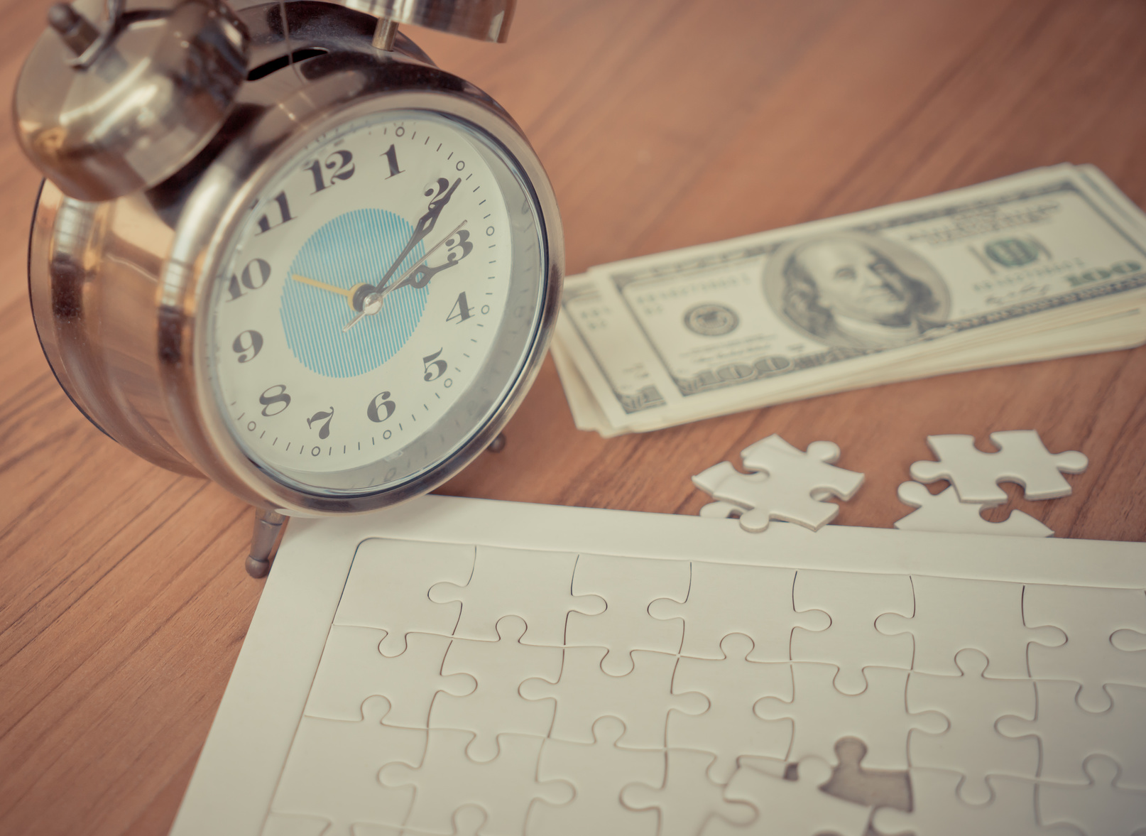 Jigsaw puzzle, hundred dollar bills, and alarm clock on wood table